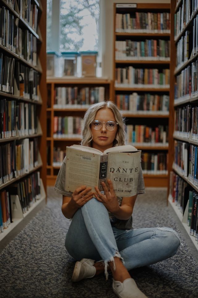 a woman sitting on the floor reading a book in a library with many bookshelves