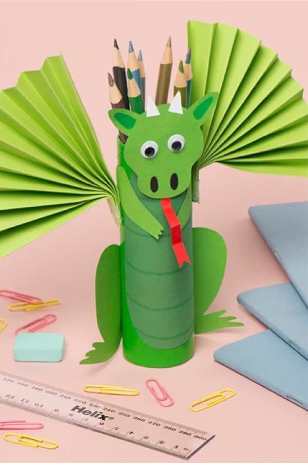 a green paper dragon sitting on top of a table next to scissors and pencils