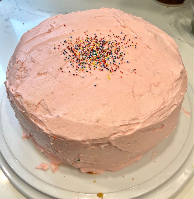 a cake with pink frosting and sprinkles on it sitting on a plate