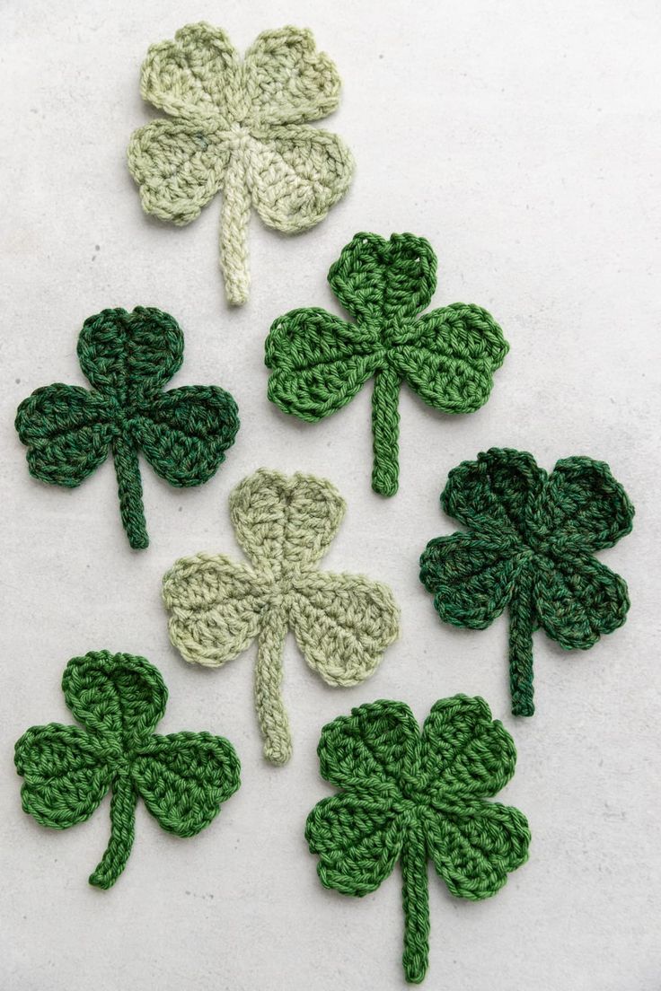 four crocheted shamrocks are arranged on a white surface with one green clover in the middle