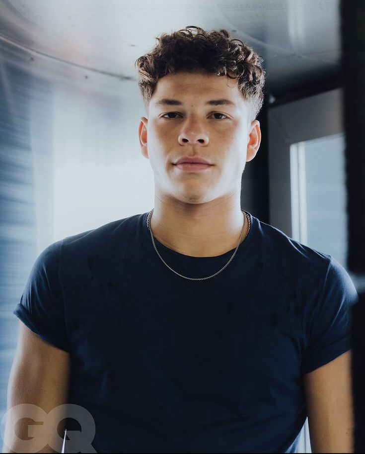 a young man in a black t - shirt is looking at the camera while wearing a necklace