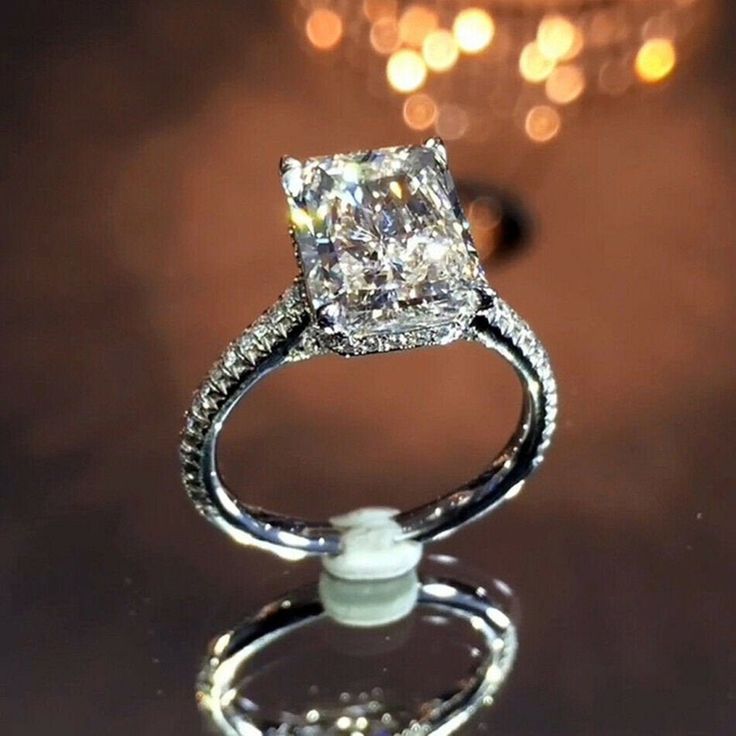 a diamond ring sitting on top of a glass table with lights in the back ground