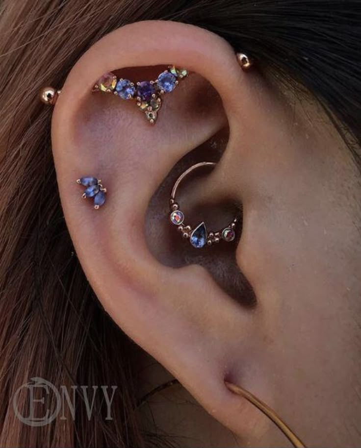 a woman wearing ear piercings with blue and clear stones on the side of her ear