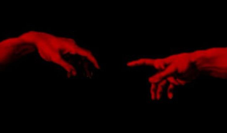 two hands reaching towards each other with red light in the dark behind them and black background