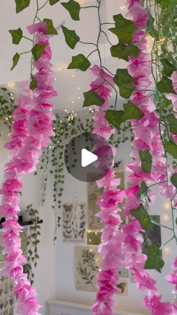 pink flowers are hanging from the ceiling in a room with white walls and green plants