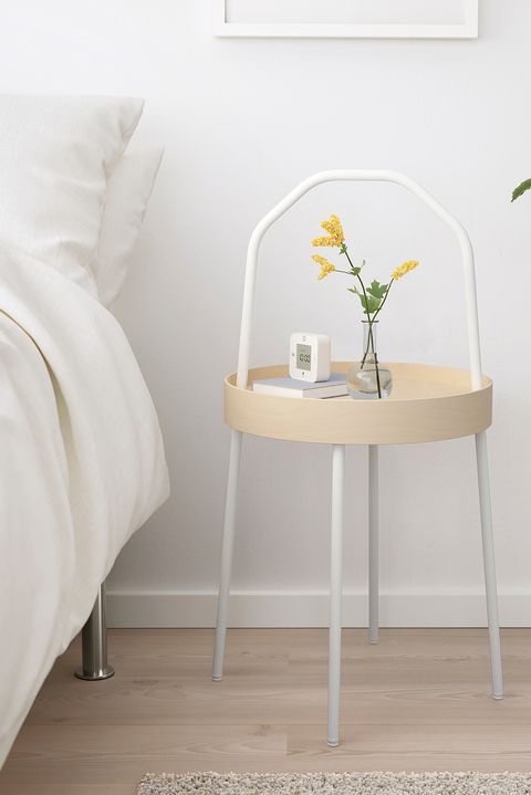 a small table with a plant on it next to a bed and a white pillow