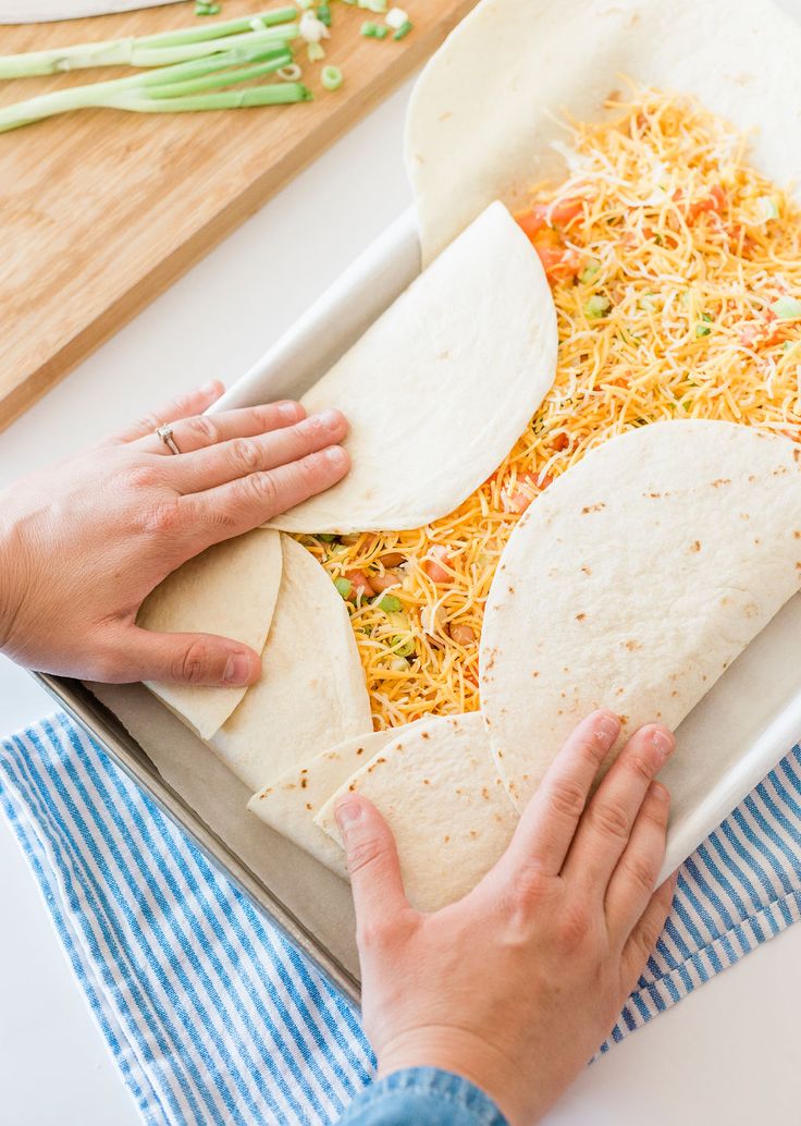 a person making tortillas with shredded cheese and vegetables in a baking pan on a counter