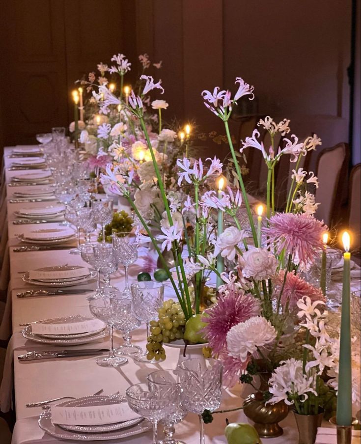 a long table is set with white and pink flowers in vases, silverware and candles