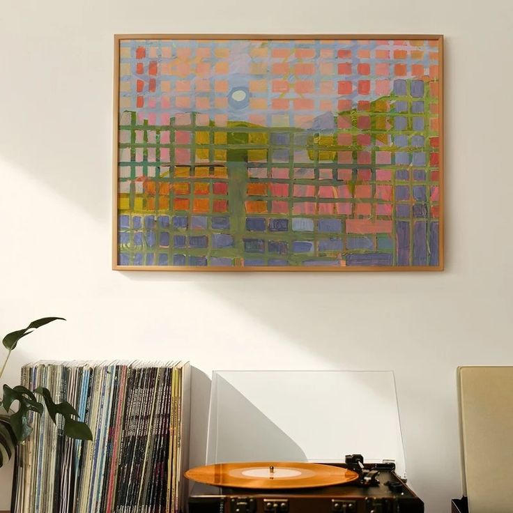 a record player sitting on top of a wooden table next to a wall mounted painting