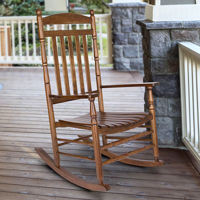 a wooden rocking chair sitting on top of a porch next to a stone wall and white railing