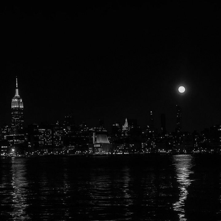 black and white photograph of the city skyline at night with full moon in sky over water