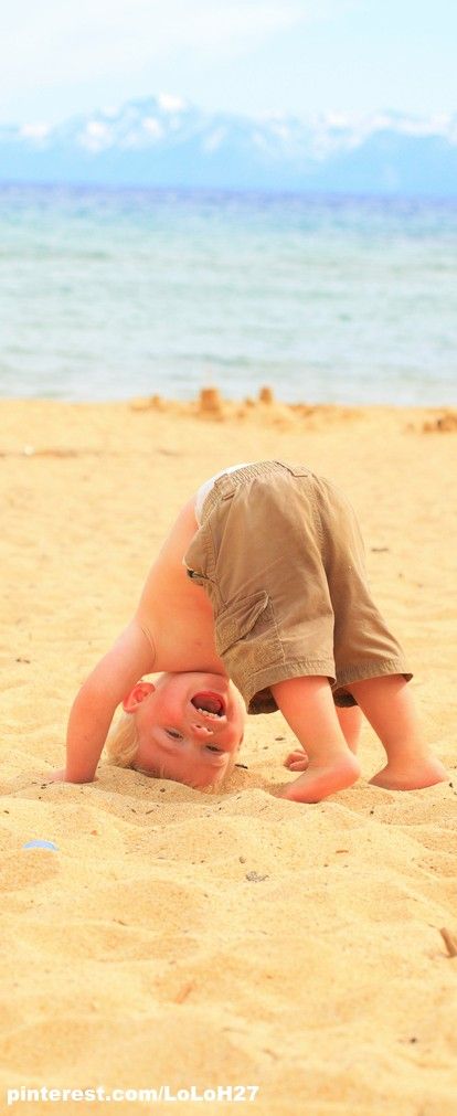 a young boy is playing in the sand at the beach with his head in the sand