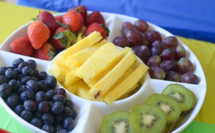 a white plate topped with fruit next to sliced kiwis and strawberries on a table