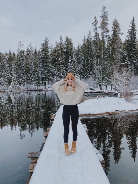 a woman standing on a dock in the snow with her hands behind her head and wearing boots