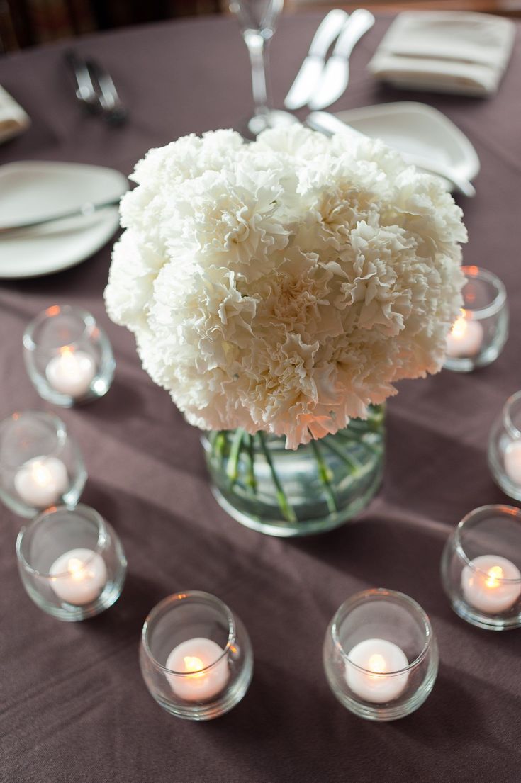 a vase filled with white flowers sitting on top of a table next to small candles