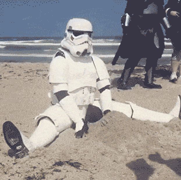 a man dressed as storm trooper sitting on the beach with other people standing behind him