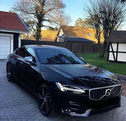 a black volvo car parked in front of a house with two garage doors on the side