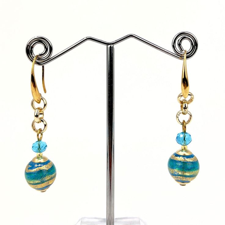 a pair of earrings with blue and gold beads on a metal stand in front of a white background