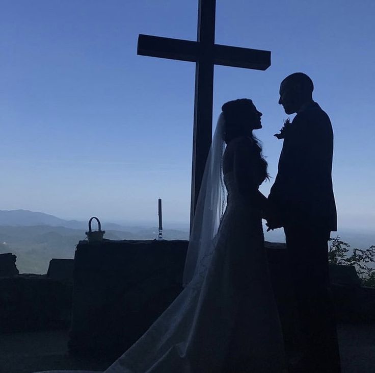 a bride and groom standing in front of a cross at the top of a hill