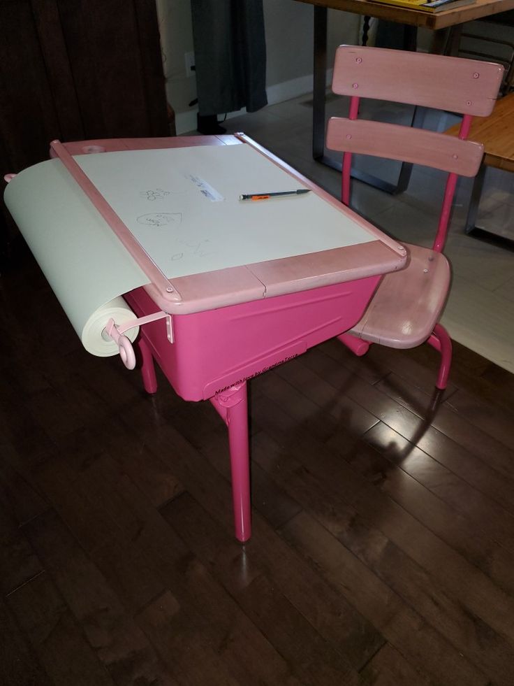 a pink table and chair with a white board on it's back end, in front of a wooden floor