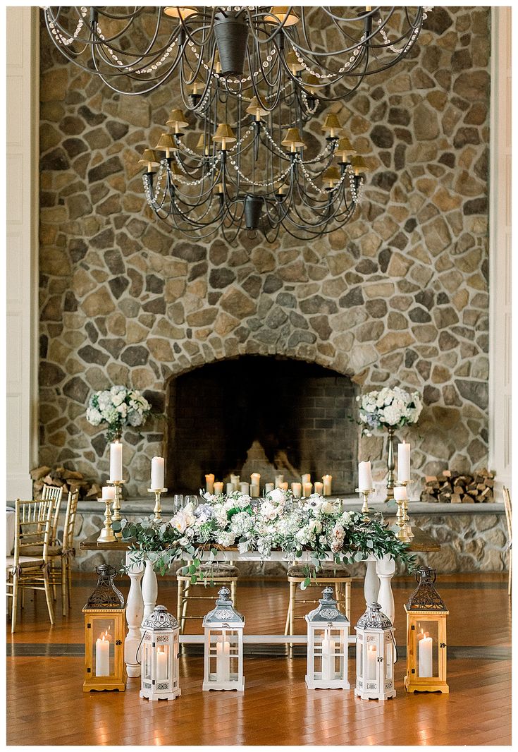 a table with candles and flowers on it in front of a stone fireplace at a wedding