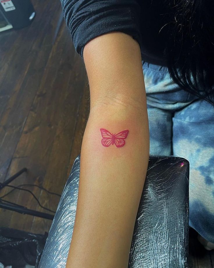 a woman's arm with a small pink butterfly tattoo on the left side of her arm