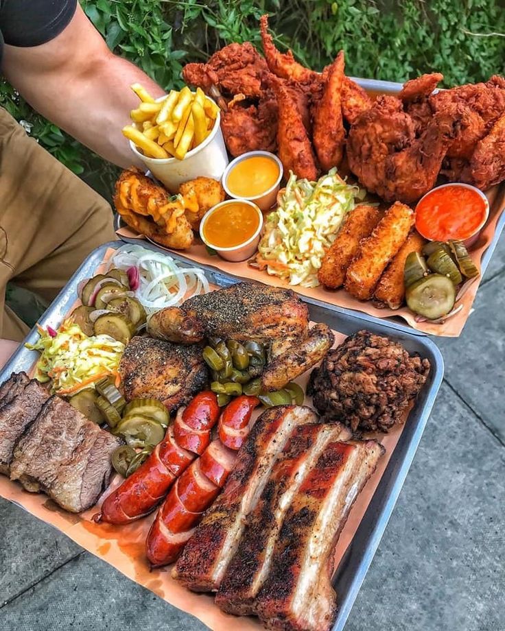 two trays filled with different types of food on top of each other next to a man's hand