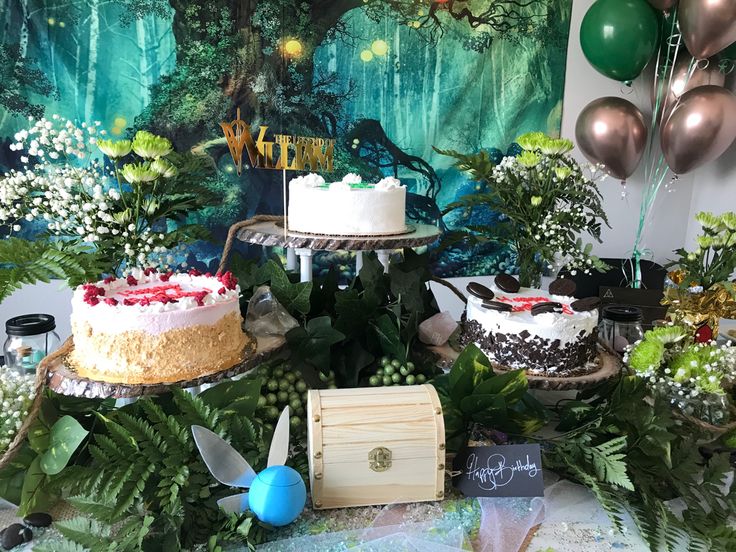 a table topped with cakes and balloons in front of a forest scene wall papered backdrop