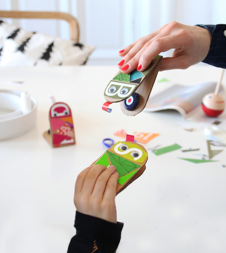 two children are playing with toy cars on the white table in front of their mother's hand