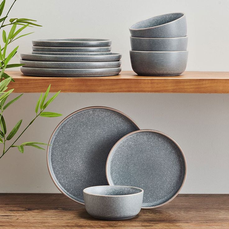 a stack of plates and bowls sitting on top of a wooden shelf next to a potted plant