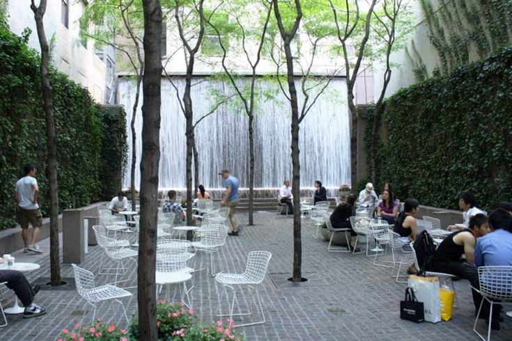 people are sitting at tables in the middle of a courtyard with trees and water fall behind them