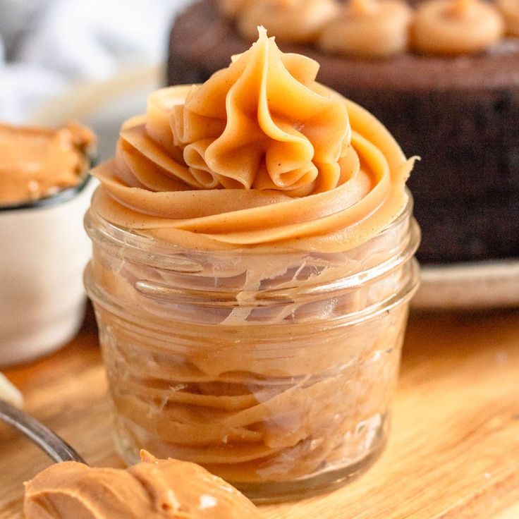 a jar filled with peanut butter on top of a wooden table next to a cake