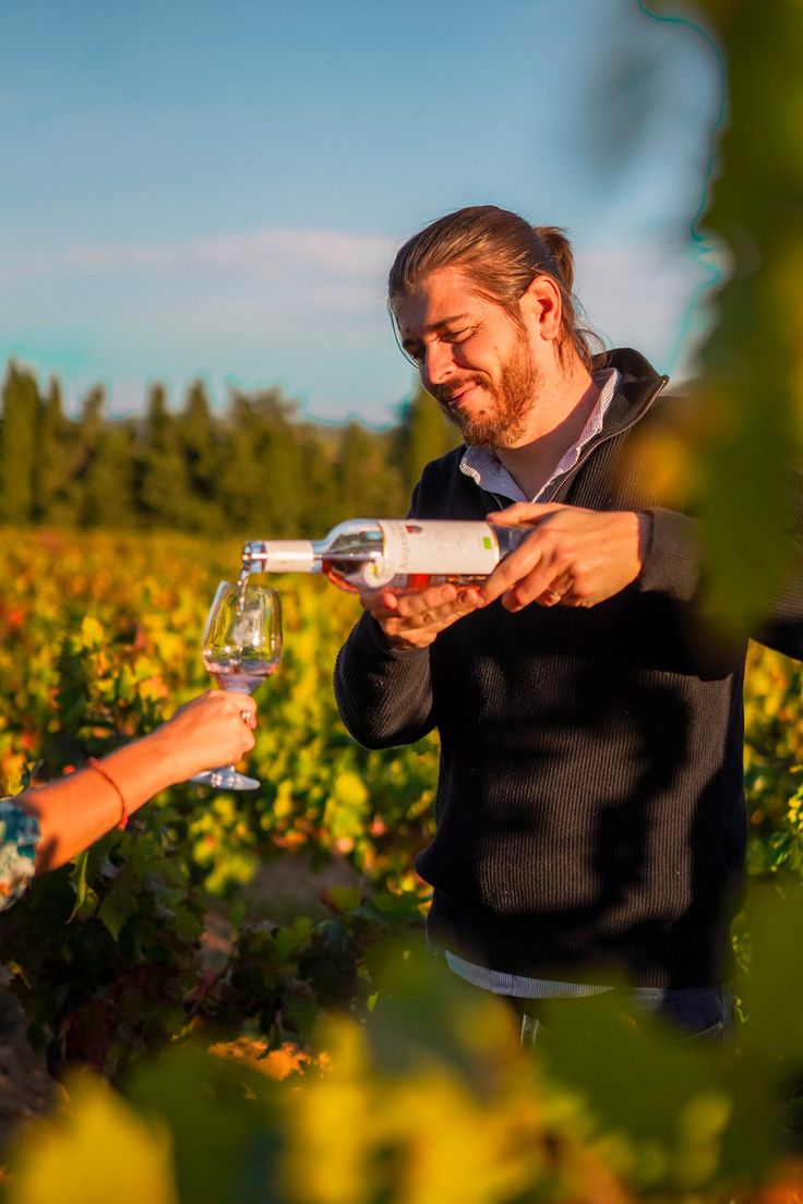 a man and woman standing in a field holding wine glasses while looking at each other