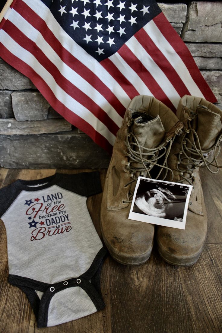 a pair of boots and a baby's bodysuit are next to an american flag