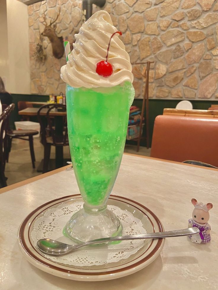 a green drink with whipped cream and a cherry on top sits on a table in a restaurant