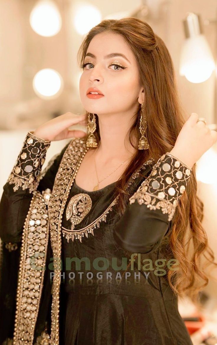 a beautiful woman in black dress posing for the camera with her hand on her shoulder