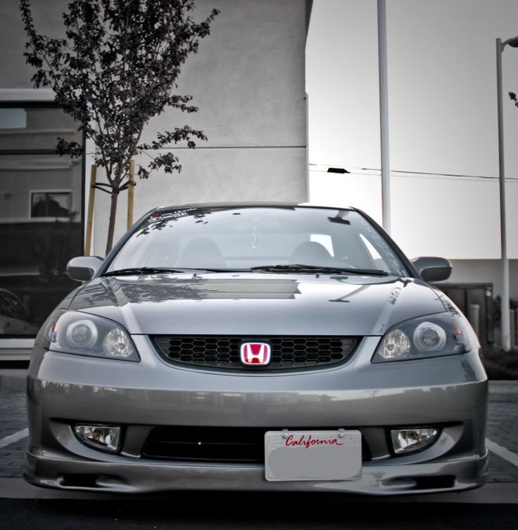 the front end of a silver car parked in a parking lot next to a building