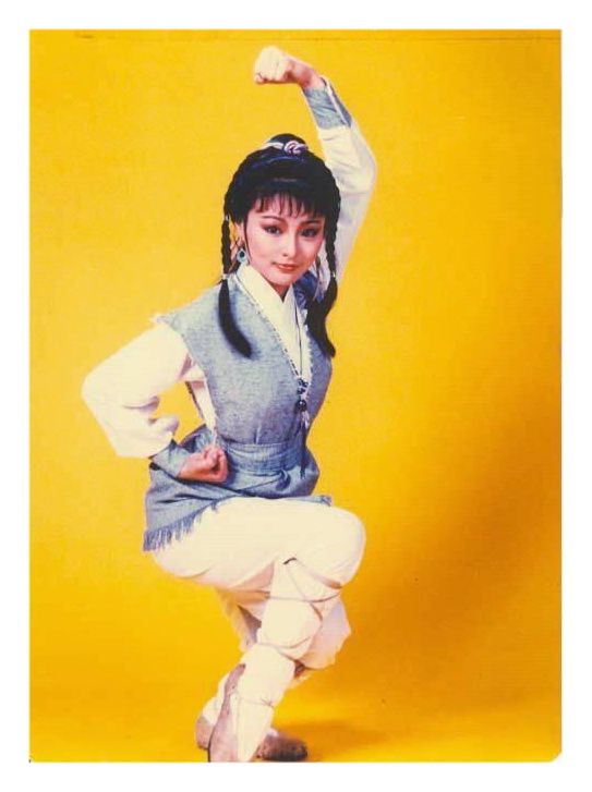 a woman is posing for a photo in white pants and a blue vest with her arms up