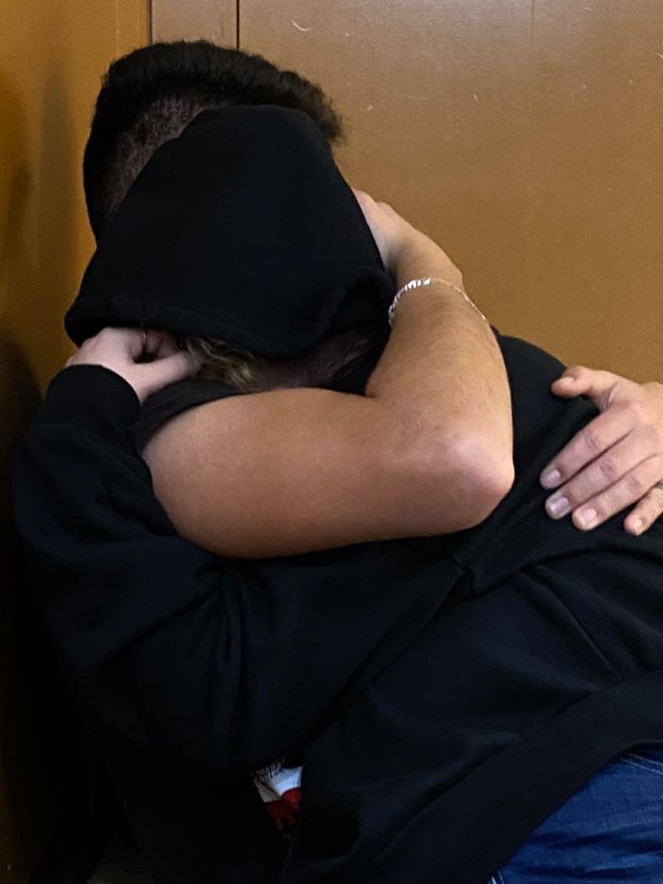 two people are hugging each other while sitting on the floor in front of a wall