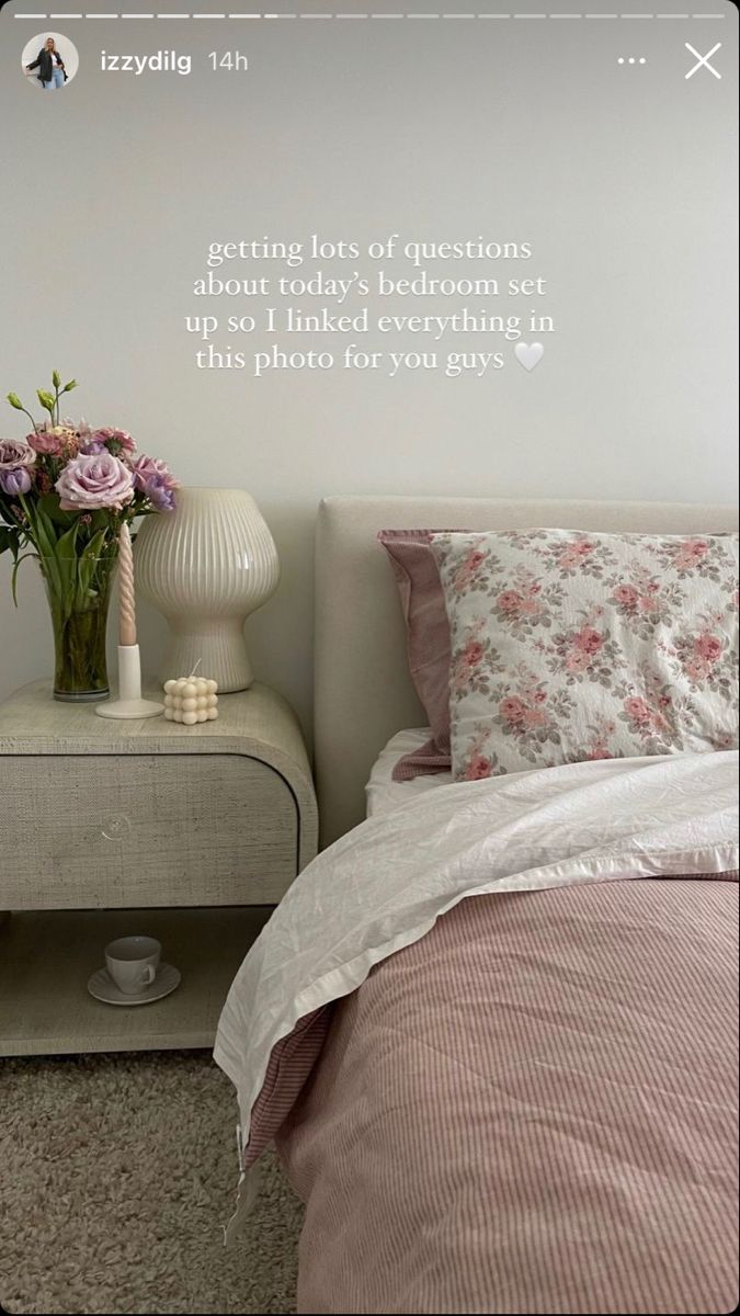 a bed with pink and white flowers on it next to a night stand that has a vase full of flowers