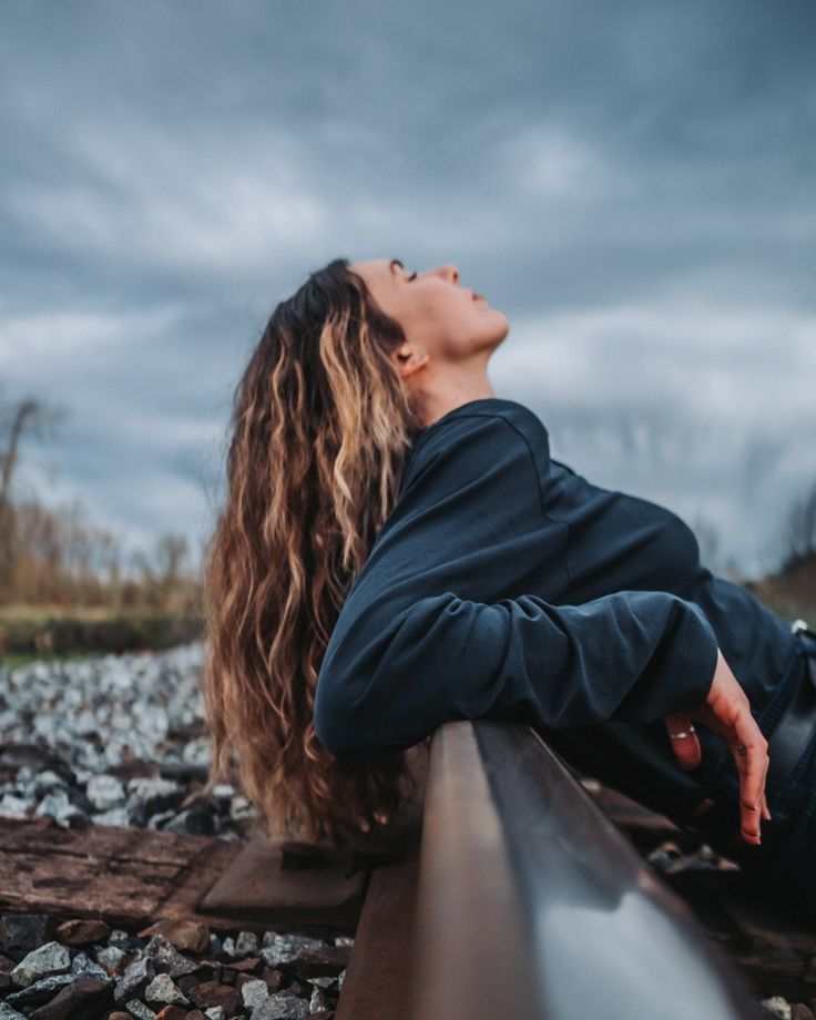 a woman with long hair sitting on a rail looking up at the sky and rocks