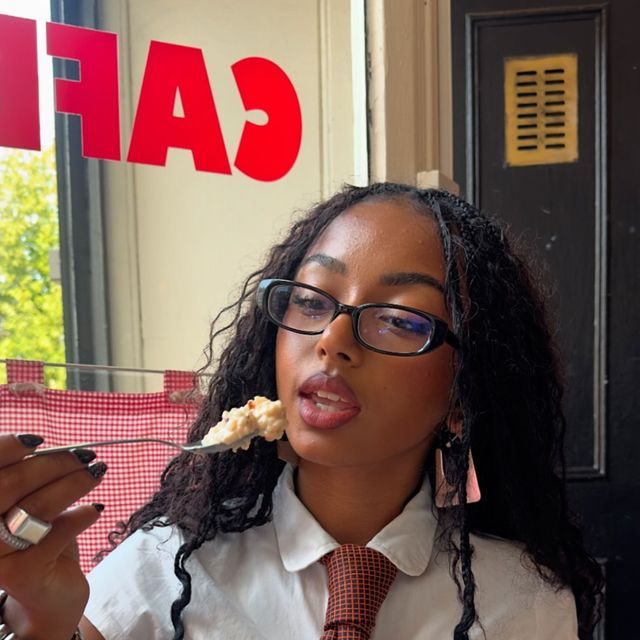 a woman wearing glasses eating food in front of a cafe sign