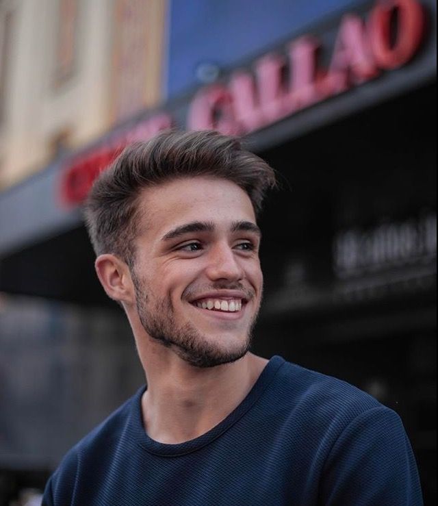 a young man smiles while standing in front of a building