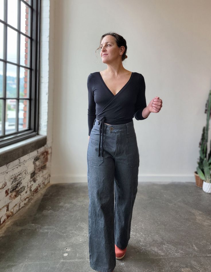 a woman standing in front of a window with her hands on her hips and looking off to the side