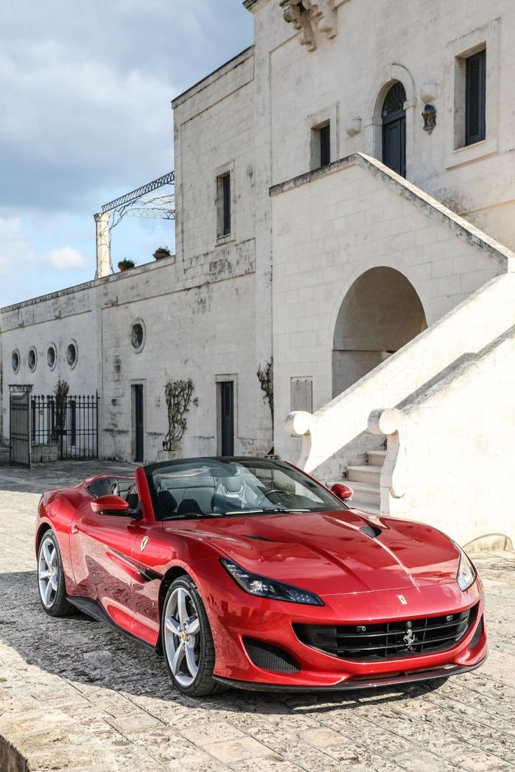 a red sports car parked in front of a white building with steps leading up to it