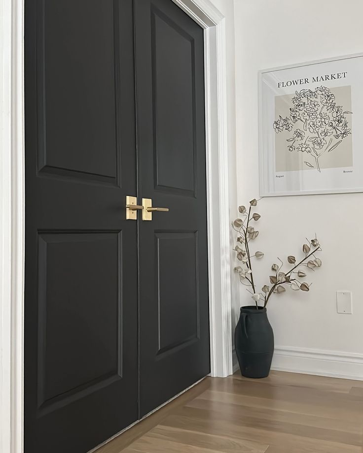 a vase with flowers in it sitting on the floor next to a black front door