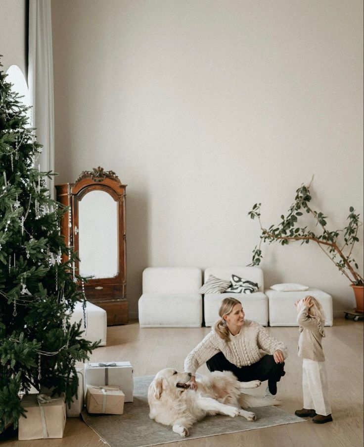 a woman sitting on the floor with her dog next to a christmas tree and presents