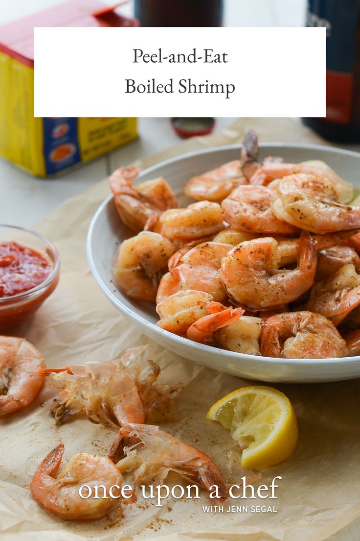 a bowl filled with cooked shrimp next to lemon wedges and ketchup sauce