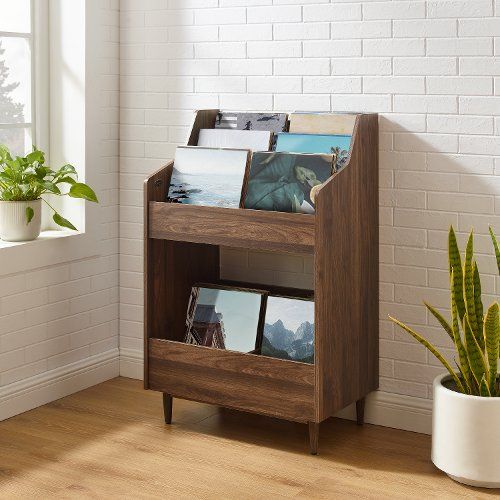 a wooden shelf with pictures and photos on it next to a potted plant in front of a white brick wall