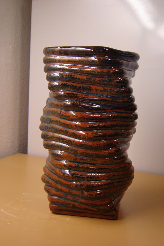 a brown vase sitting on top of a yellow table next to a white wall and a window